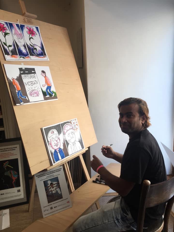 ARiF drawing at an easel, surrounded by original cartoon artwork